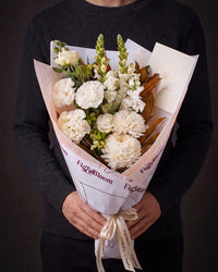 The Toast, the Pyrenees Gesture bouquet held at chest height with the greeting card tucked into the wrap, against a charcoal backdrop.