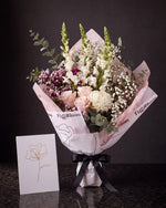 The Wish, the Osaka Gesture bouquet tied with black ribbon, standing on dark stone beside the Single Stem greeting card.