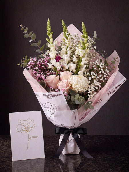 The Wish, the Osaka Gesture bouquet tied with black ribbon, standing on dark stone beside the Single Stem greeting card.